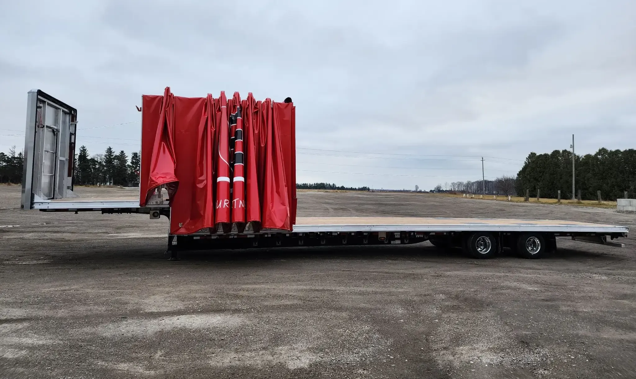 A Titan tarp system retracted to the front of a flatbed trailer, leaving the deck open for loading